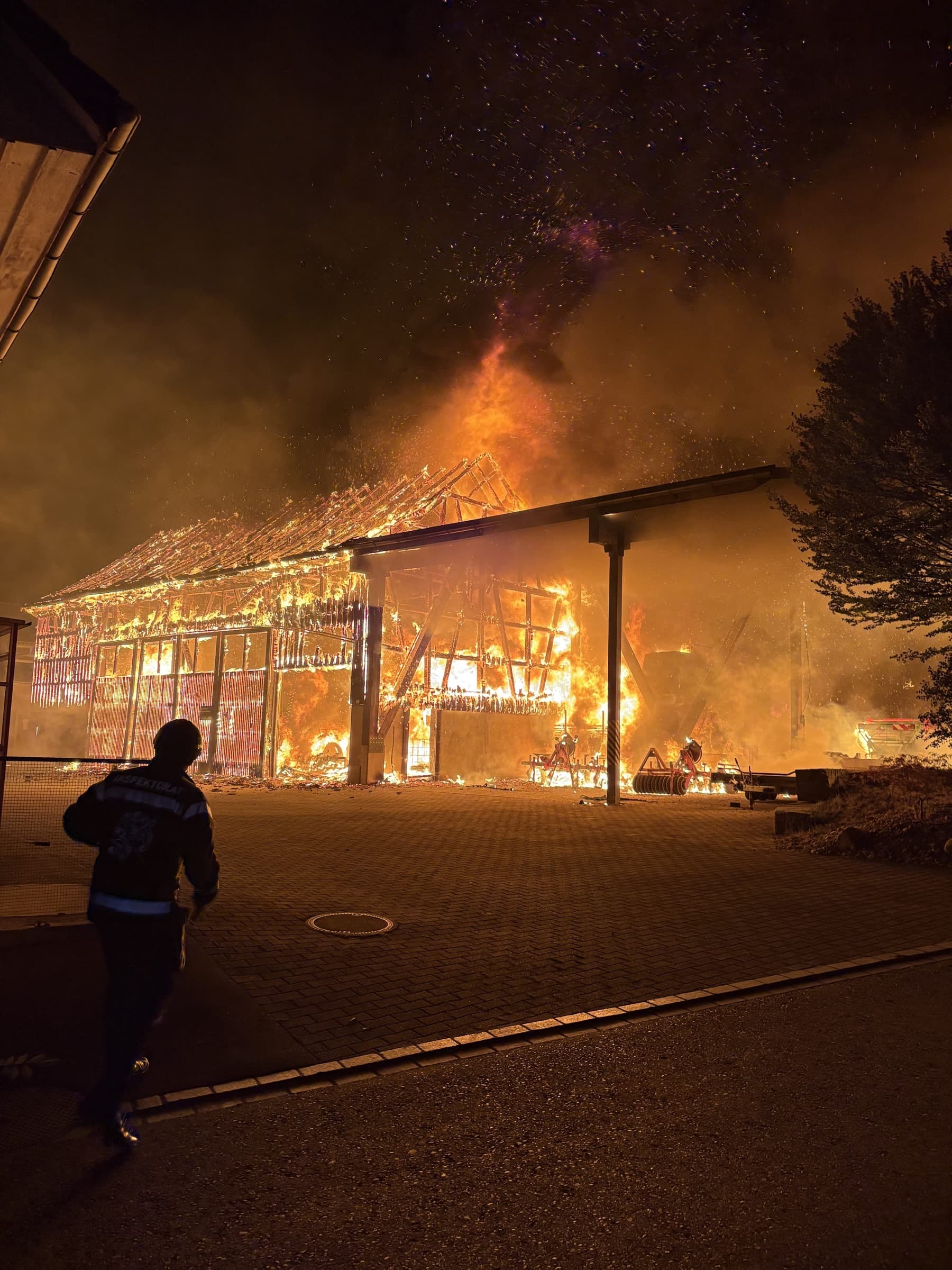 Die brennende Maschinenhalle in Neuwilen in der Nacht, im Vordergrund eine Einsatzkraft