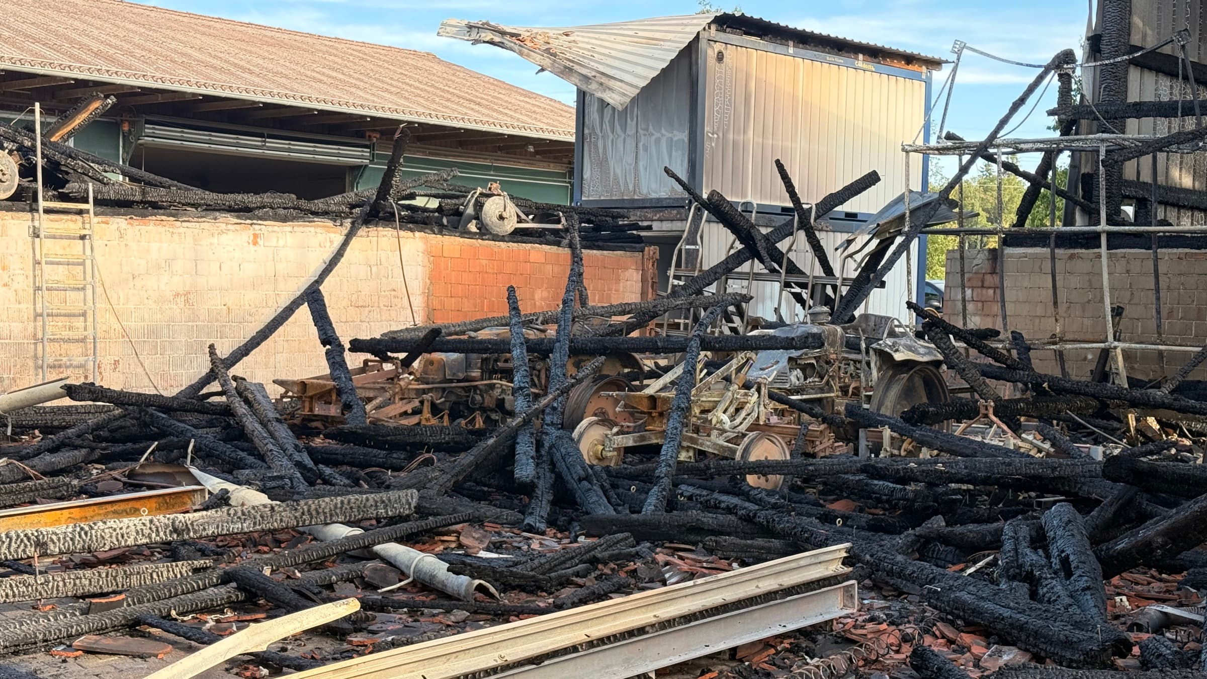 Verkohlte Dachbalken und zerstörte Landmaschinen auf dem Brandplatz